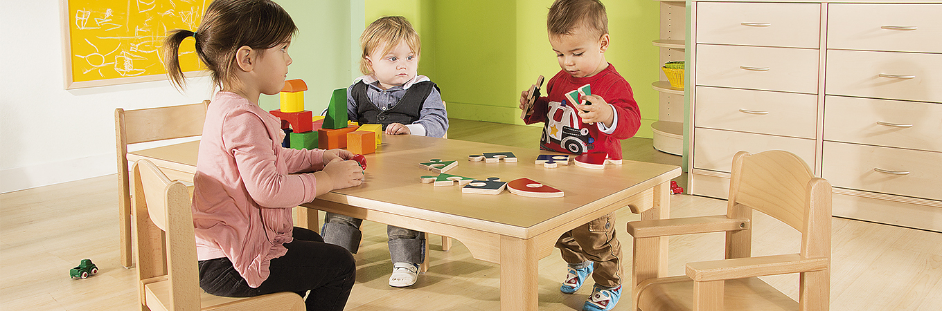 Kinder sitzen an Kindergartentisch und spielen gemeinsam