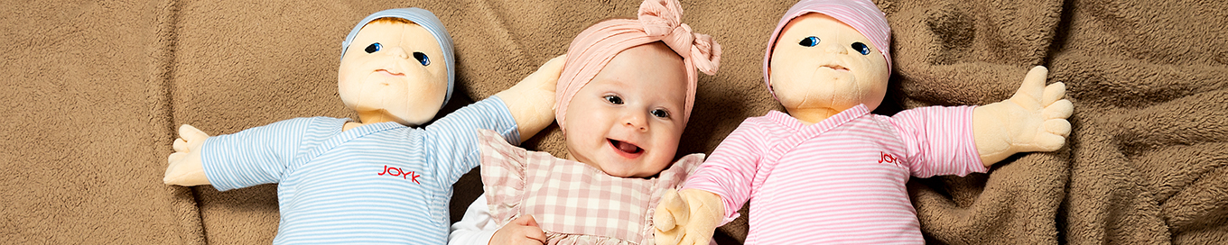 Ein Baby liegt zwischen zwei Baby-Puppen