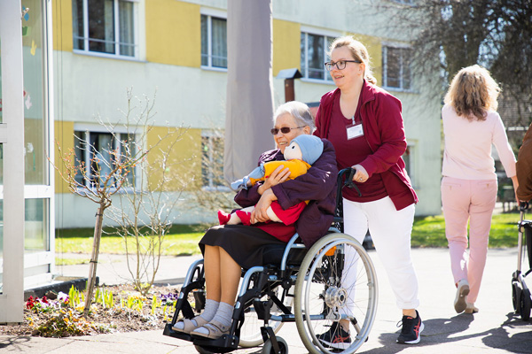 Seniorin im Rollstuhl hält Puppe Ingrid im Arm