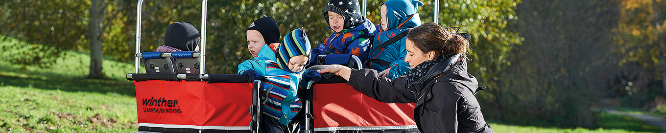 Eine Erzieherin ist mit Kindern im Transportwagen bei einem Spaziergang