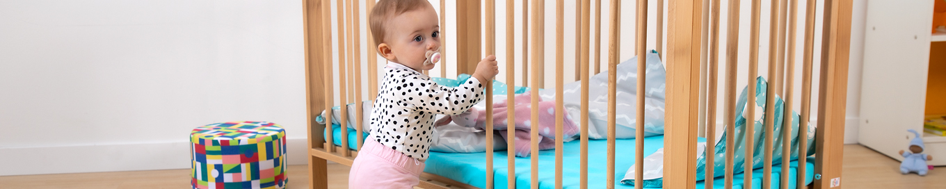 Ein Baby hält sich an den Stäben eines Krippenbettes fest