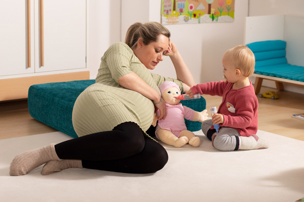 Schwangere Mutter mit Kind und Neugeborenen Empathiepuppe beim Füttern