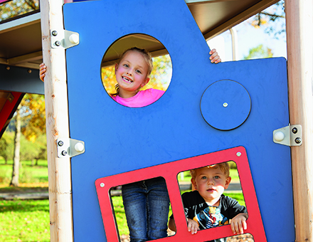 Dusyma Kindergarten Spielplatz Kinder schauen durch eine Dusyma Spielplatzwand mit Gucklöchern