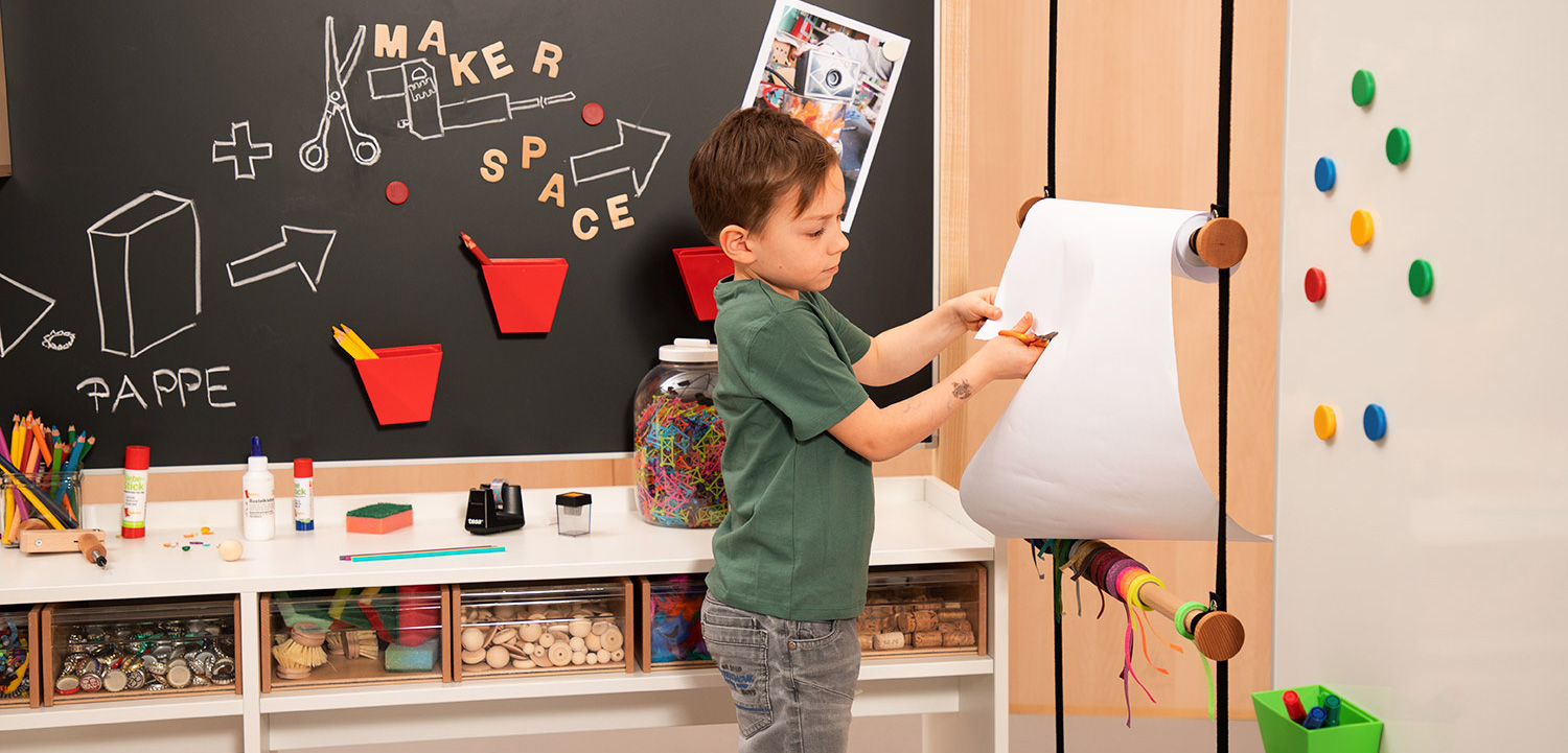 Kind zeichnet an einer hängenden Papierrolle Makerspace