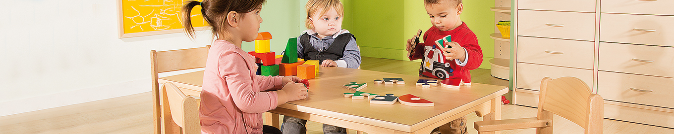 Drei Kinder sitzen auf Stühlen an einem Gruppentisch